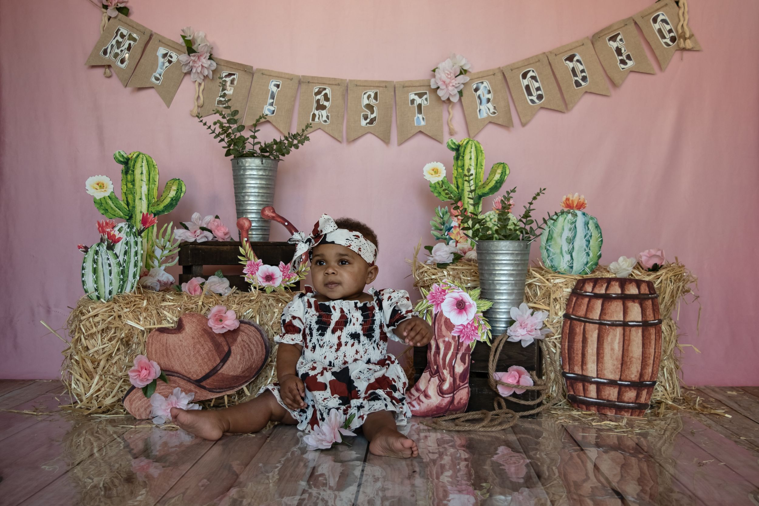 Western themed party decoration display with cactus props, wooden barrels, and rustic bunting against a pink backdrop.