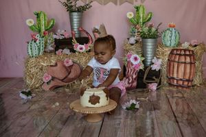 A festive cake smash photo setup with cactus decorations, pink backdrop, and rustic wooden floor.