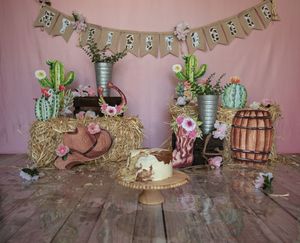 Rustic party decor setup with cactus decorations, wooden barrels, and floral accents against a pink backdrop.