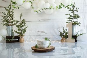 Rustic winter centerpiece with evergreen branches and white candles arranged on wooden boards with a white backdrop.