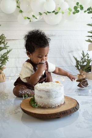 Sequence of photos showing a cake smash session with decorative greenery and white balloons in the background.