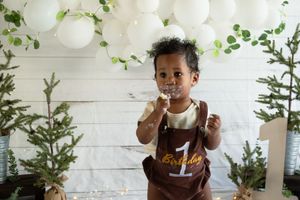 Festive winter party setup with white balloons and small evergreen trees against rustic white wooden backdrop.