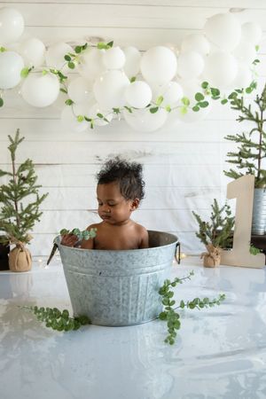 Rustic metal tub bath setup with evergreen branches and white balloon decorations.