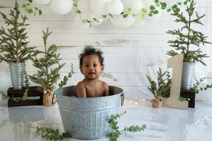 Decorative bath scene with metal tub surrounded by white balloons and pine tree branches.