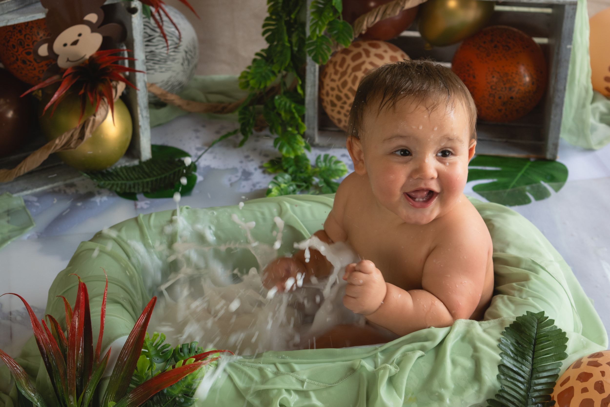 A baby sits among Christmas decorations and greenery with a joyful expression.