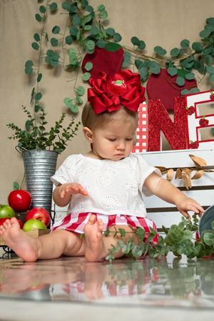 White dress and red bow against eucalyptus branches and holiday decorations.