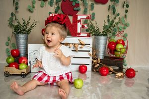 A baby plays with green apples while sitting in a rustic farmhouse-themed photo setup.