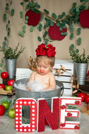 Rustic holiday photo setup with red and white checkered decorations, silver buckets, greenery and apples as props.