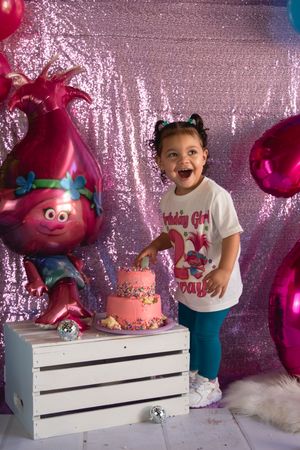 Pink and blue themed birthday party setup with sparkly backdrop and decorative balloons against a white platform.