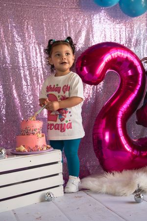 Birthday celebration setup with pink sparkly backdrop, blue and pink balloons, and white platform against shimmery wall.