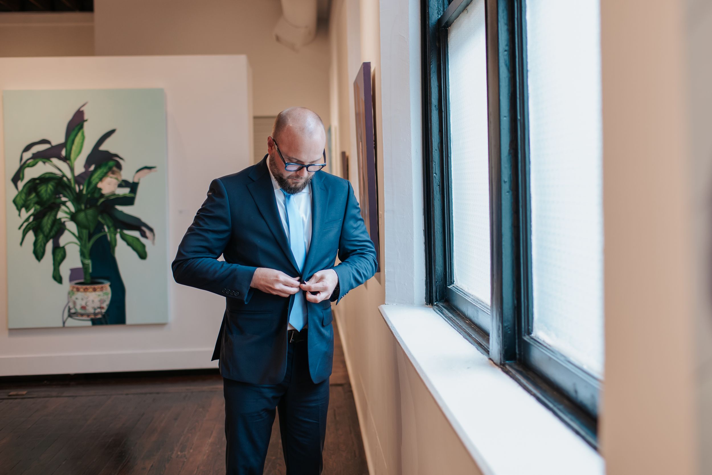 Professional wearing a blue suit jacket checks their phone while standing in a bright office space near windows.