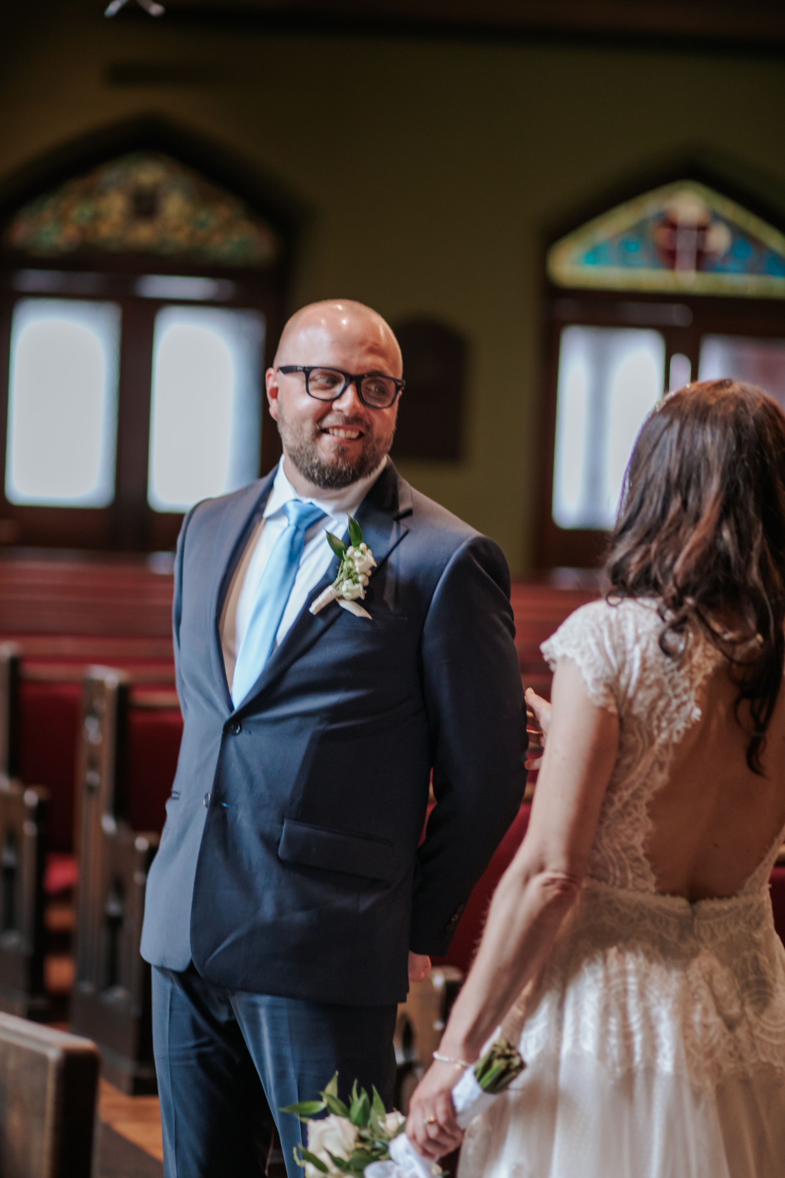 A couple shares a moment during their wedding ceremony inside a historic church with stained glass windows.