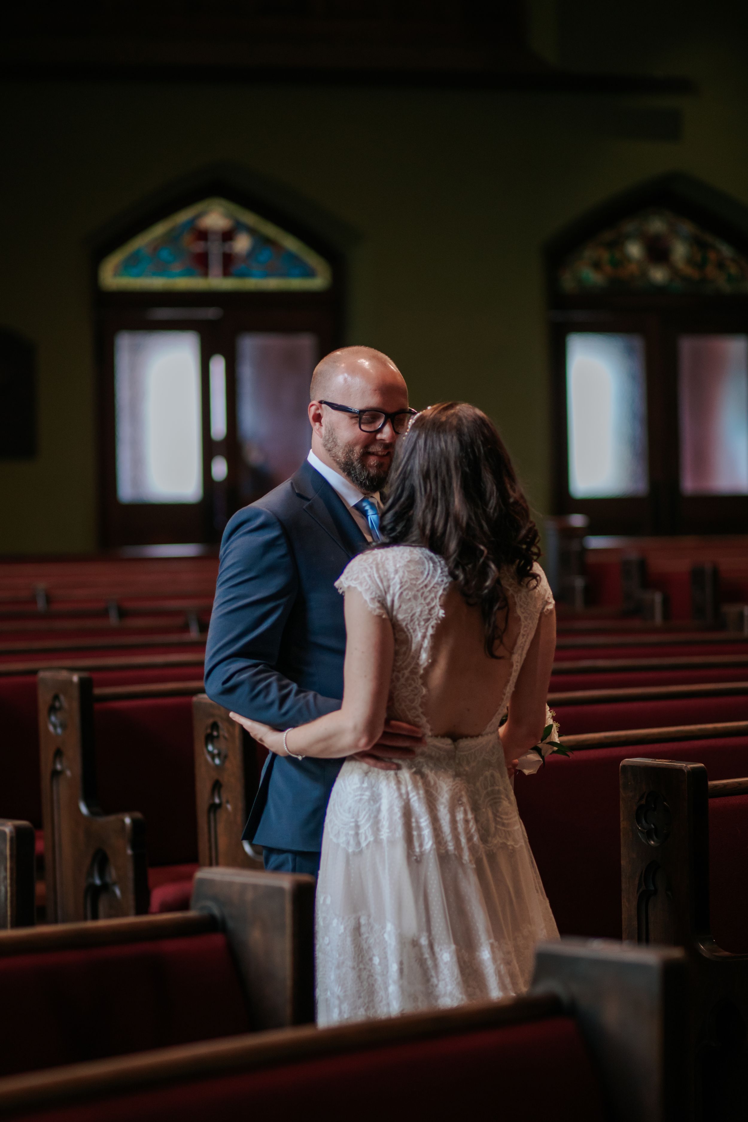 A couple shares an intimate moment together in a church sanctuary surrounded by wooden pews and stained glass windows.
