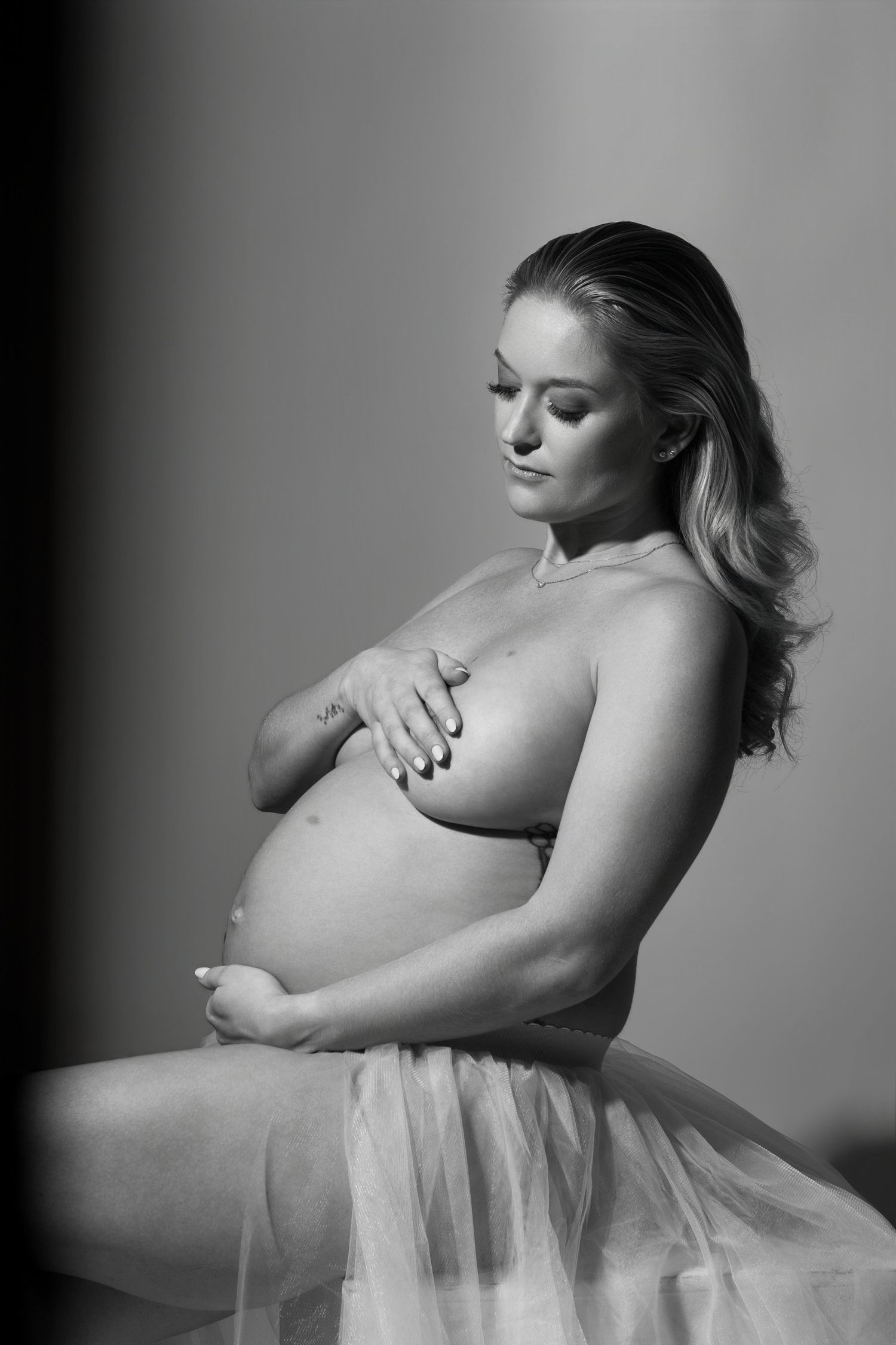 Pregnant woman in flowing blue chiffon fabric gown poses gracefully against white background.