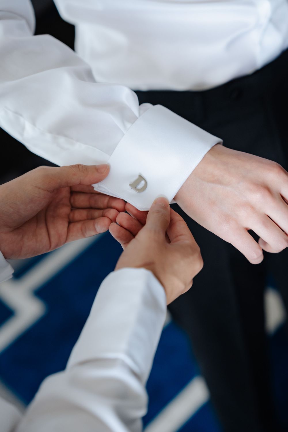 Someone fastening monogrammed cufflinks on a groom's white dress shirt sleeve.