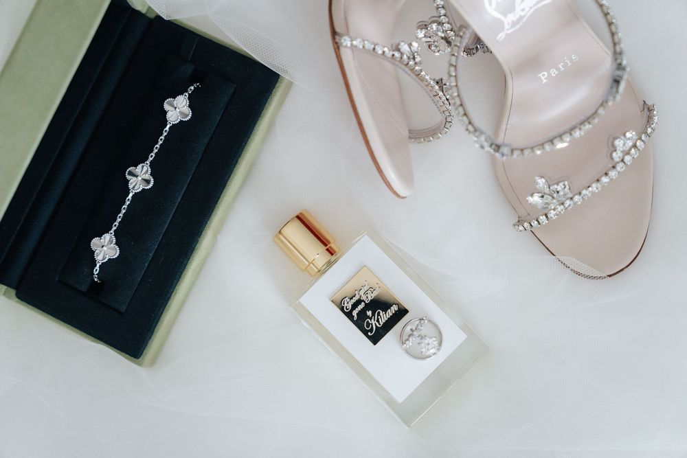 Elegant bridal accessories flat lay featuring a diamond bracelet, perfume bottle, and crystal-embellished heeled sandal.