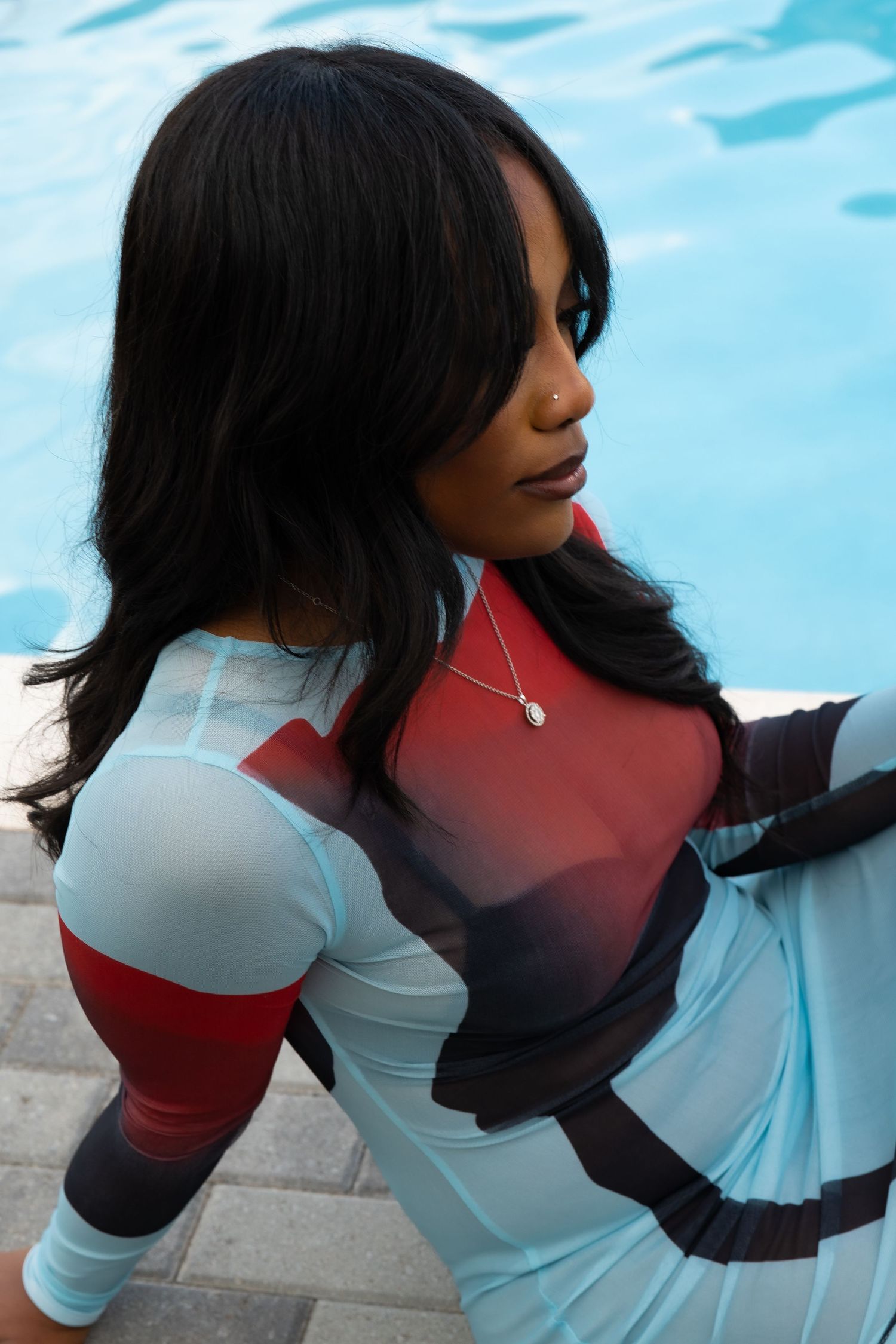 A cosplayer in a white and red bodysuit poses near a pool with long dark hair and a delicate necklace.