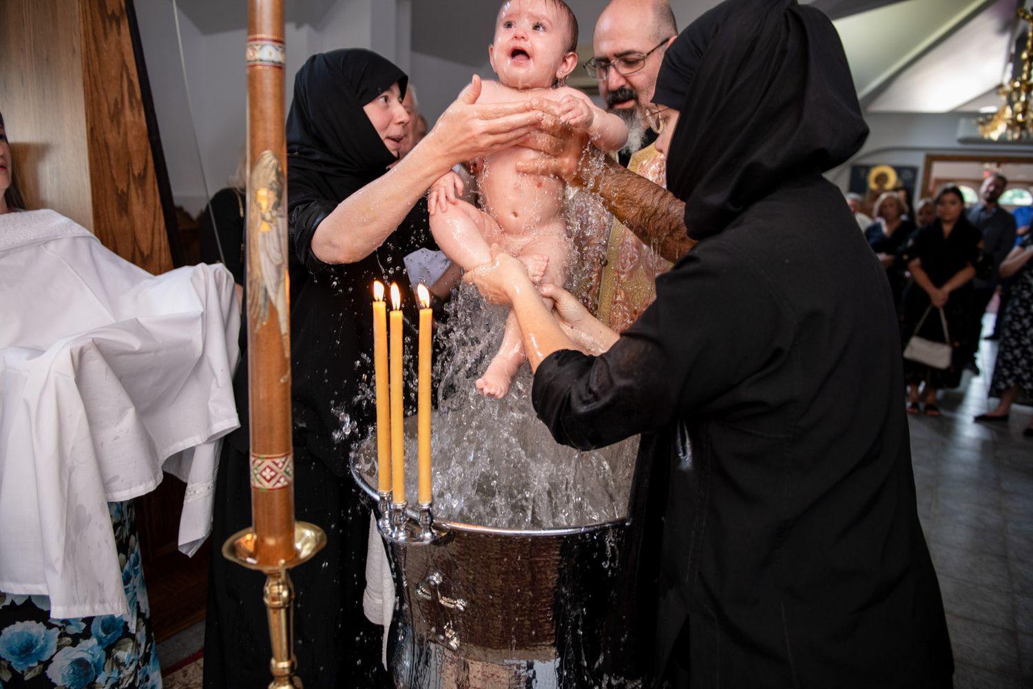 A baby being immersed in a baptismal font during an Orthodox Christian christening ceremony in a church.