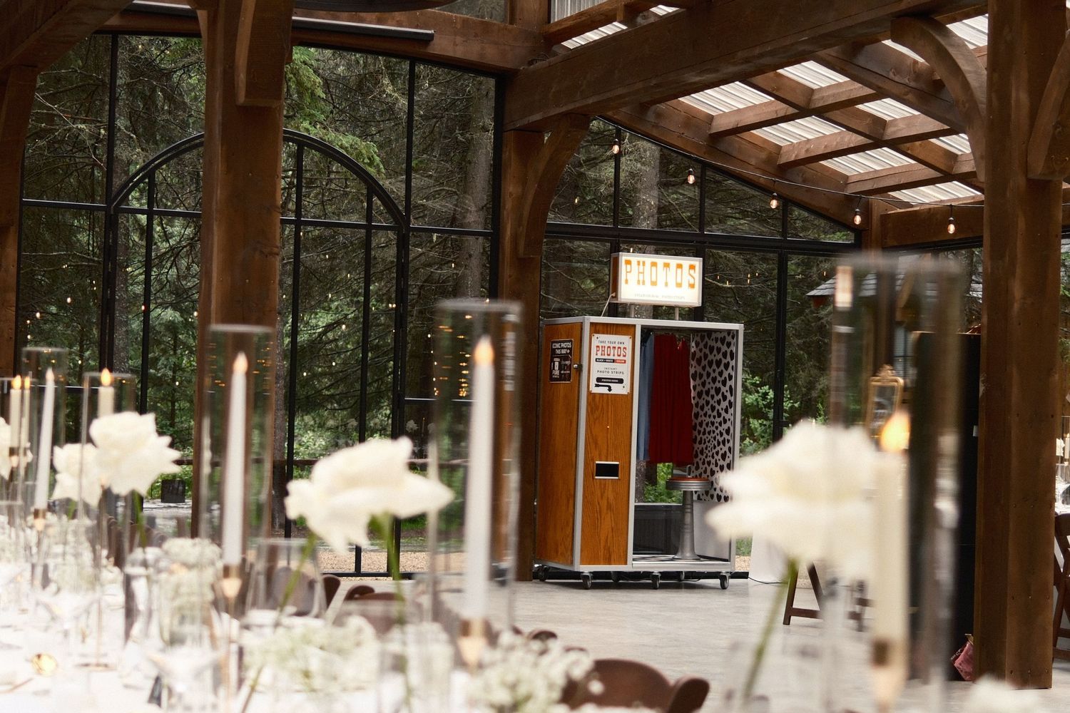 Vintage-style photo booth with red curtain, checkered floor, wood panel exterior, and illuminated PHOTOS sign on wheels.