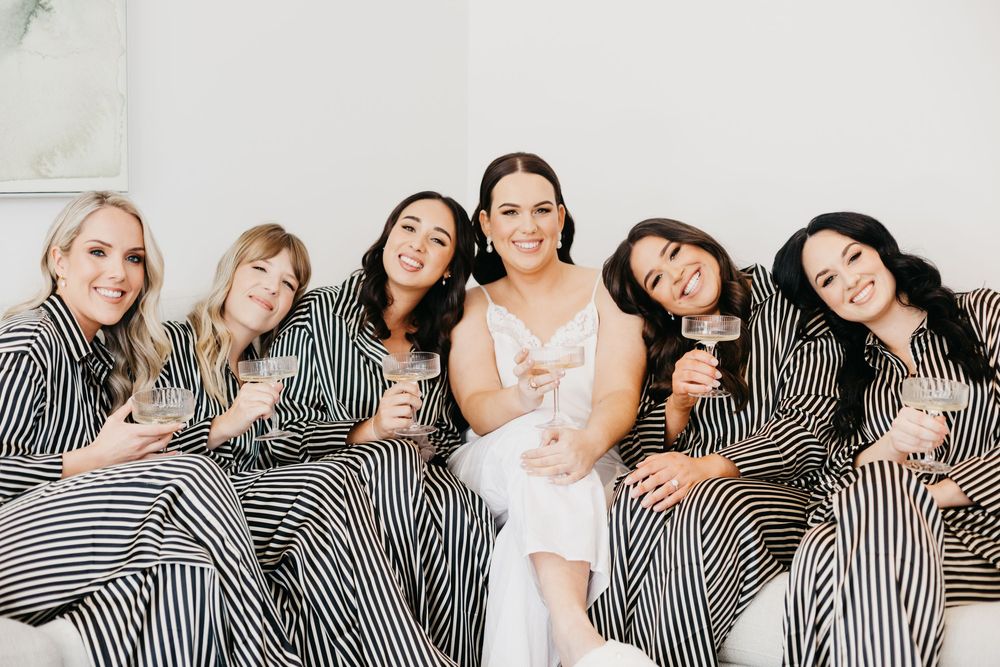 Bride in white with five bridesmaids in black stripe robes holding champagne glasses.