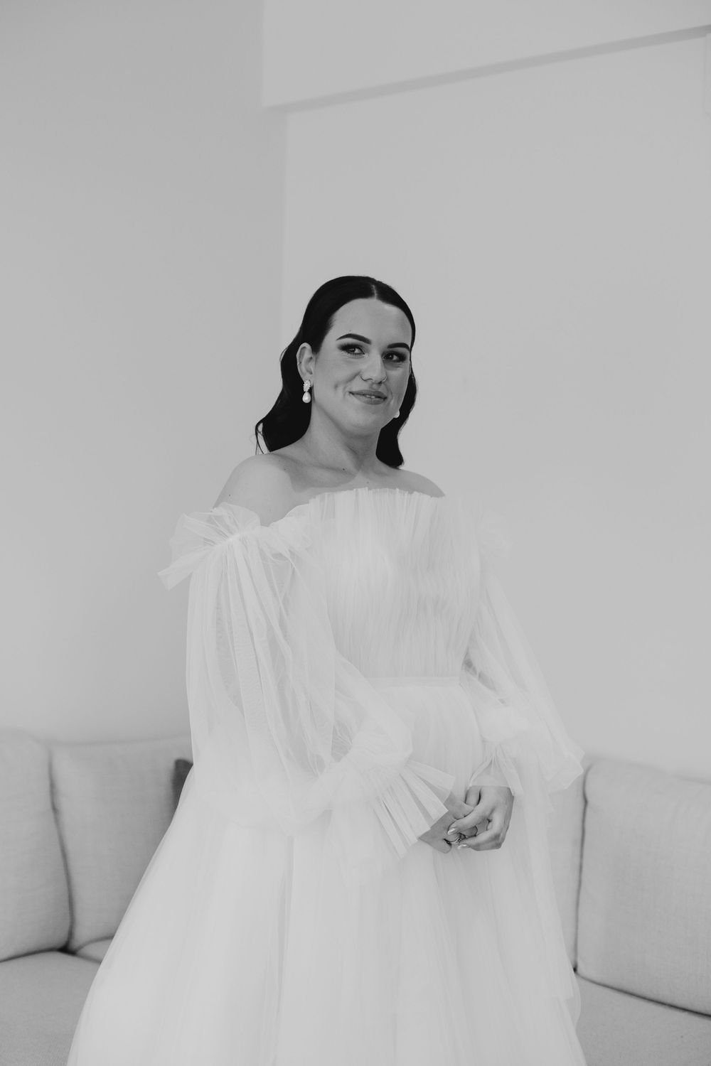 Elegant bride in off-shoulder tulle wedding gown posing in black and white portrait photo.