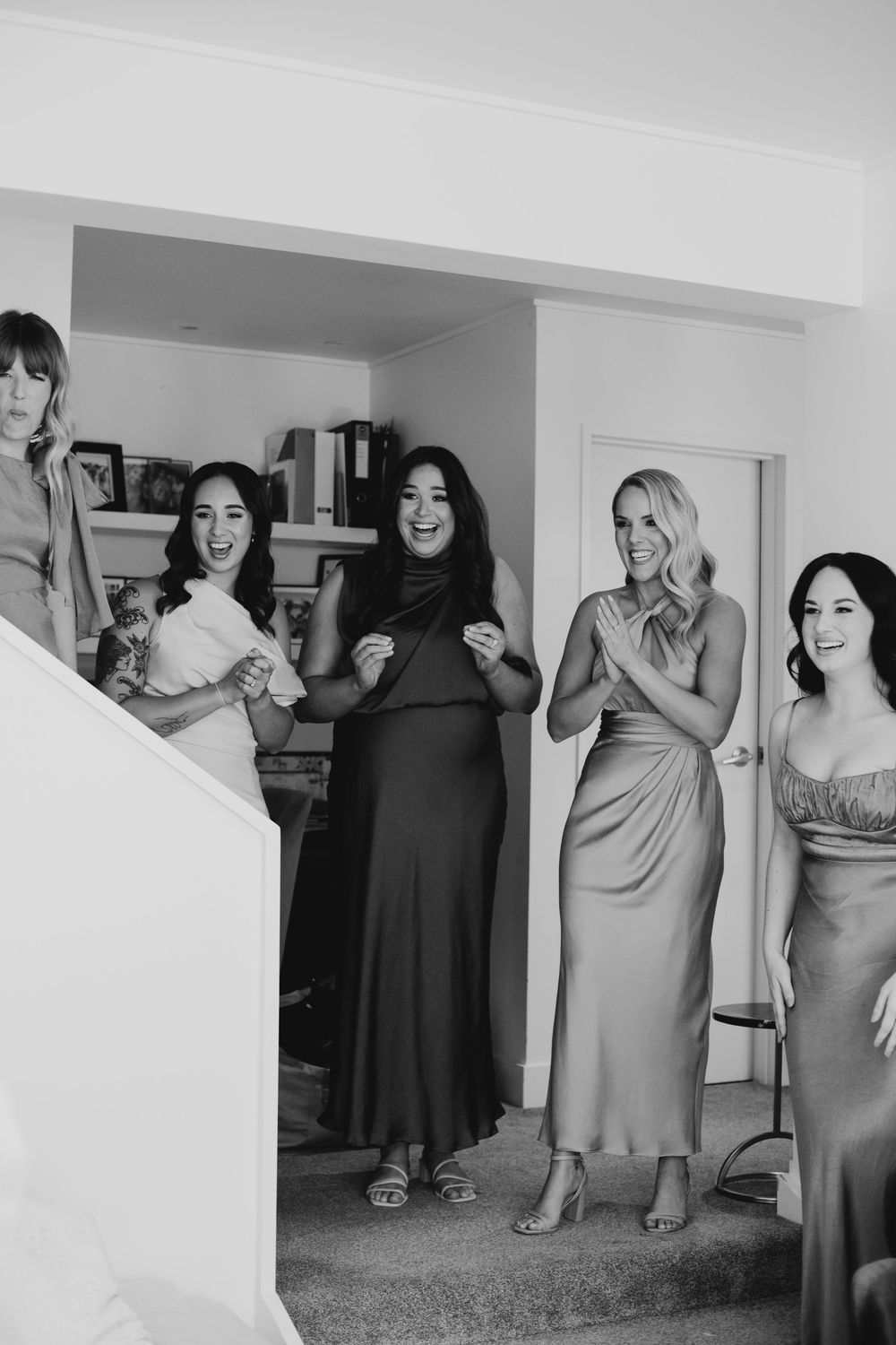 Bridesmaids reacting with joy and excitement seeing bride in wedding dress for first time.