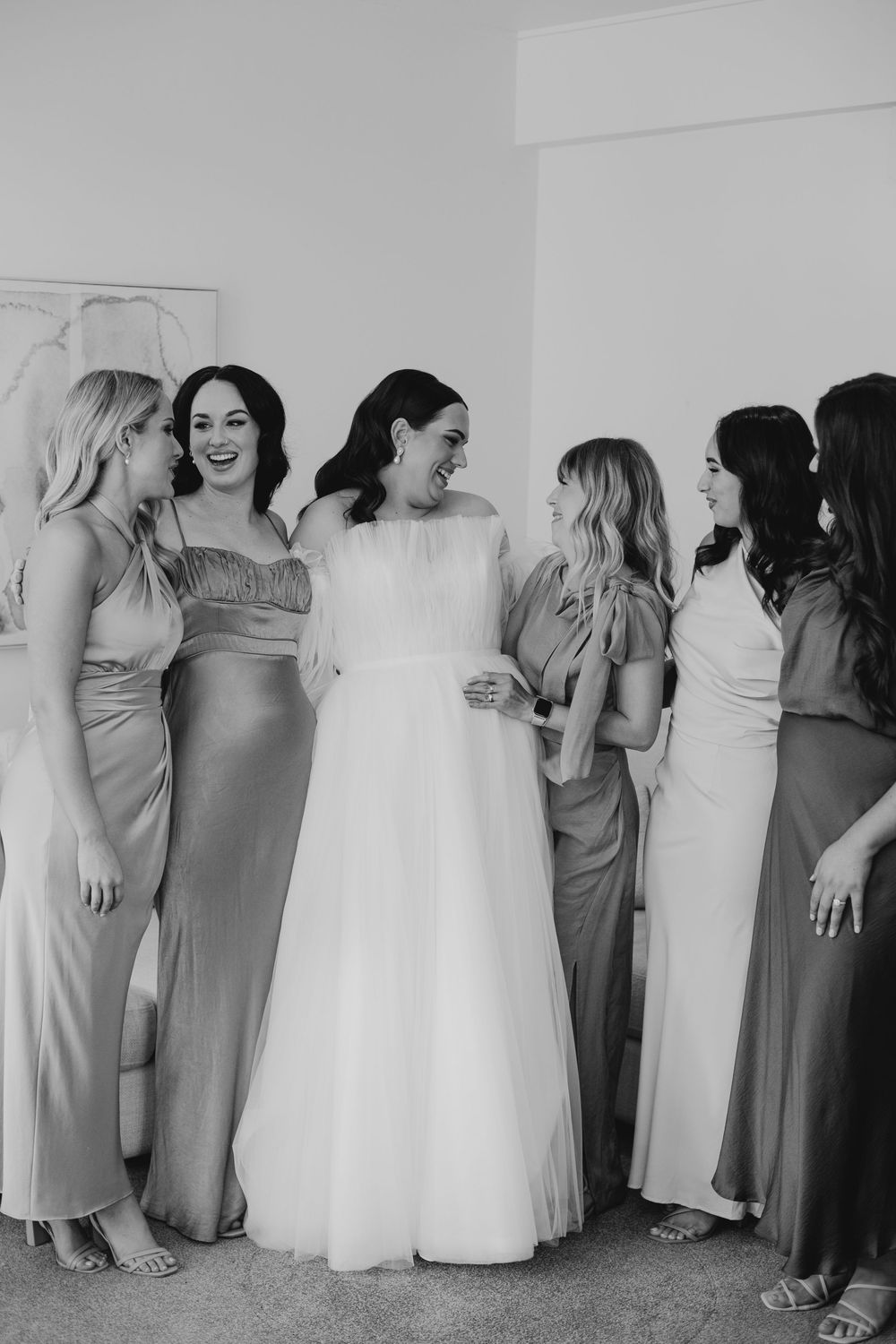 Bride in flowing tulle gown laughing with bridesmaids in mismatched satin dresses.