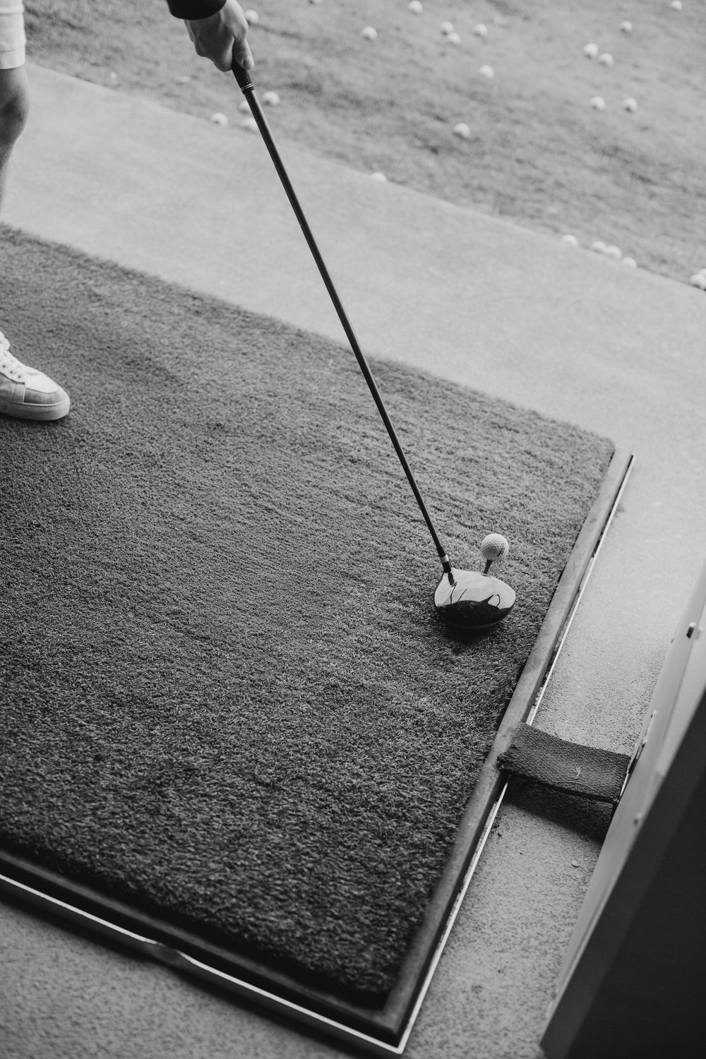 Black and white close-up of golf club addressing ball on driving range mat.