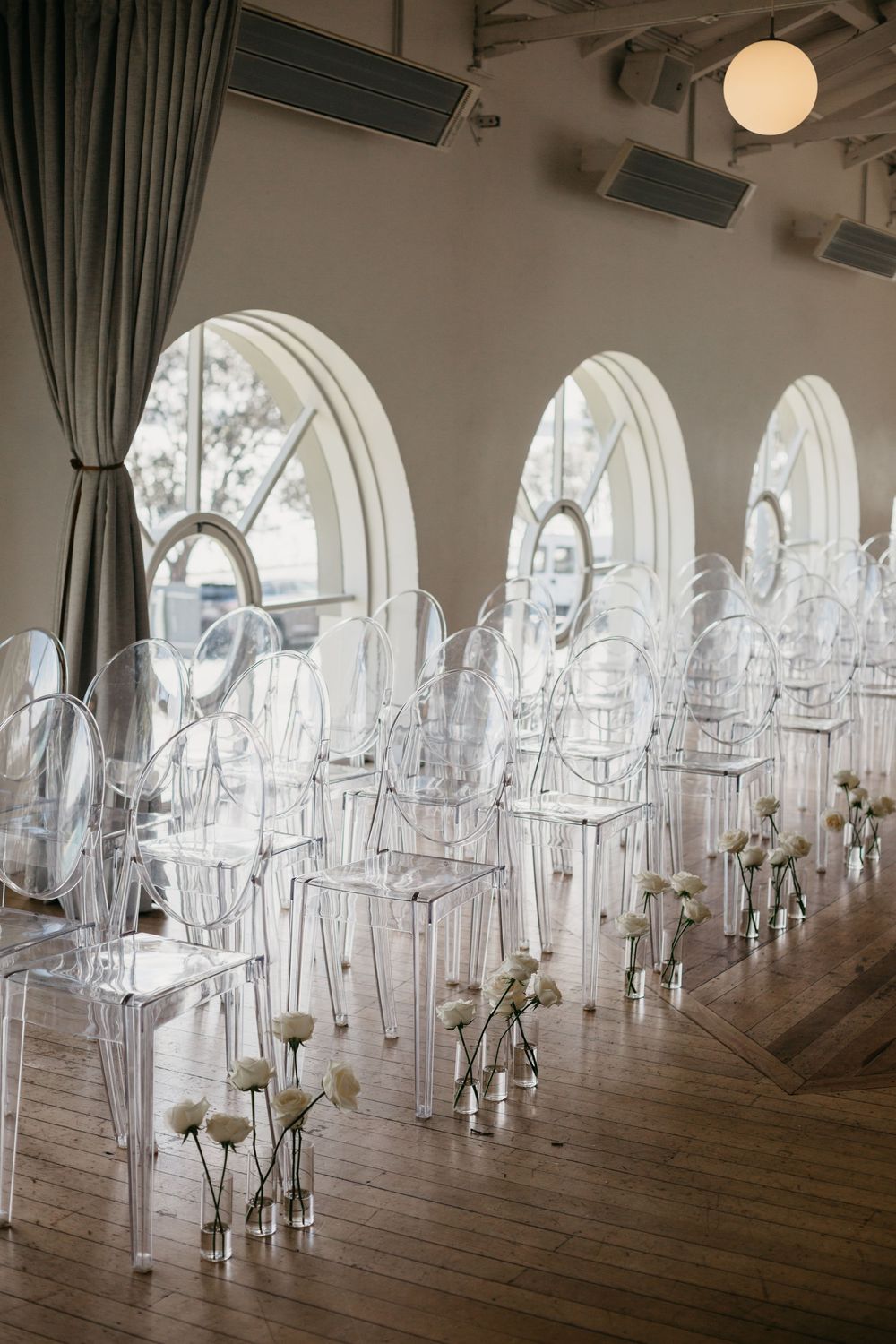 Clear ghost chairs lined up for wedding ceremony with white flowers in glass vases.