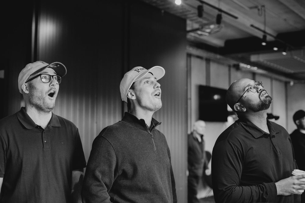 Black and white photo of three men in caps laughing and looking up indoors.