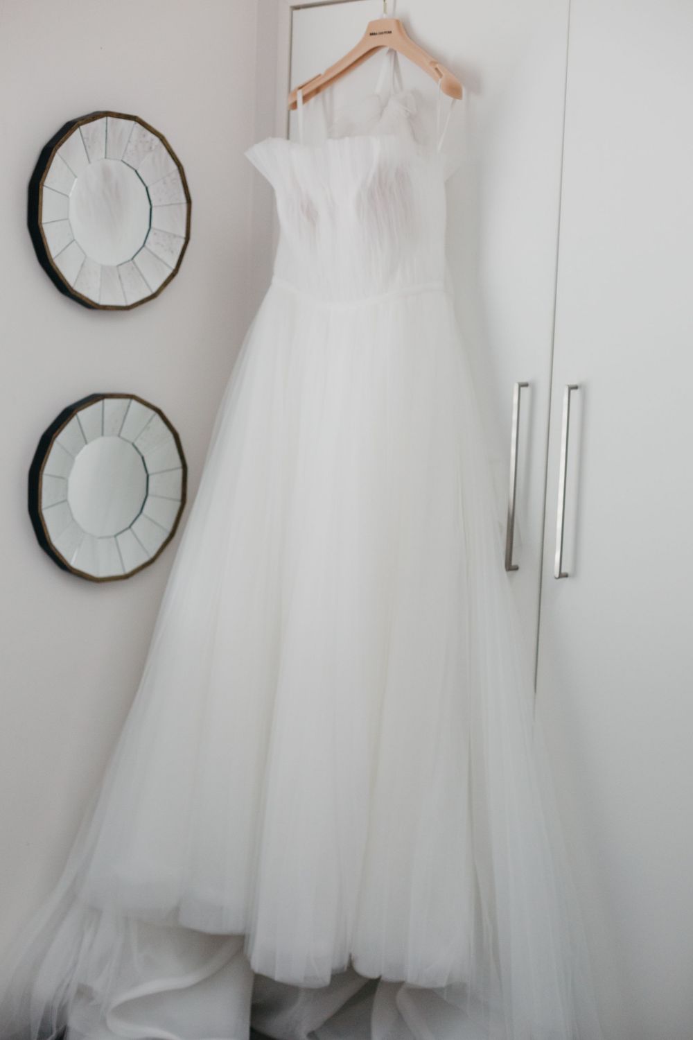 Elegant white tulle wedding dress hanging on wooden hanger against white wardrobe.