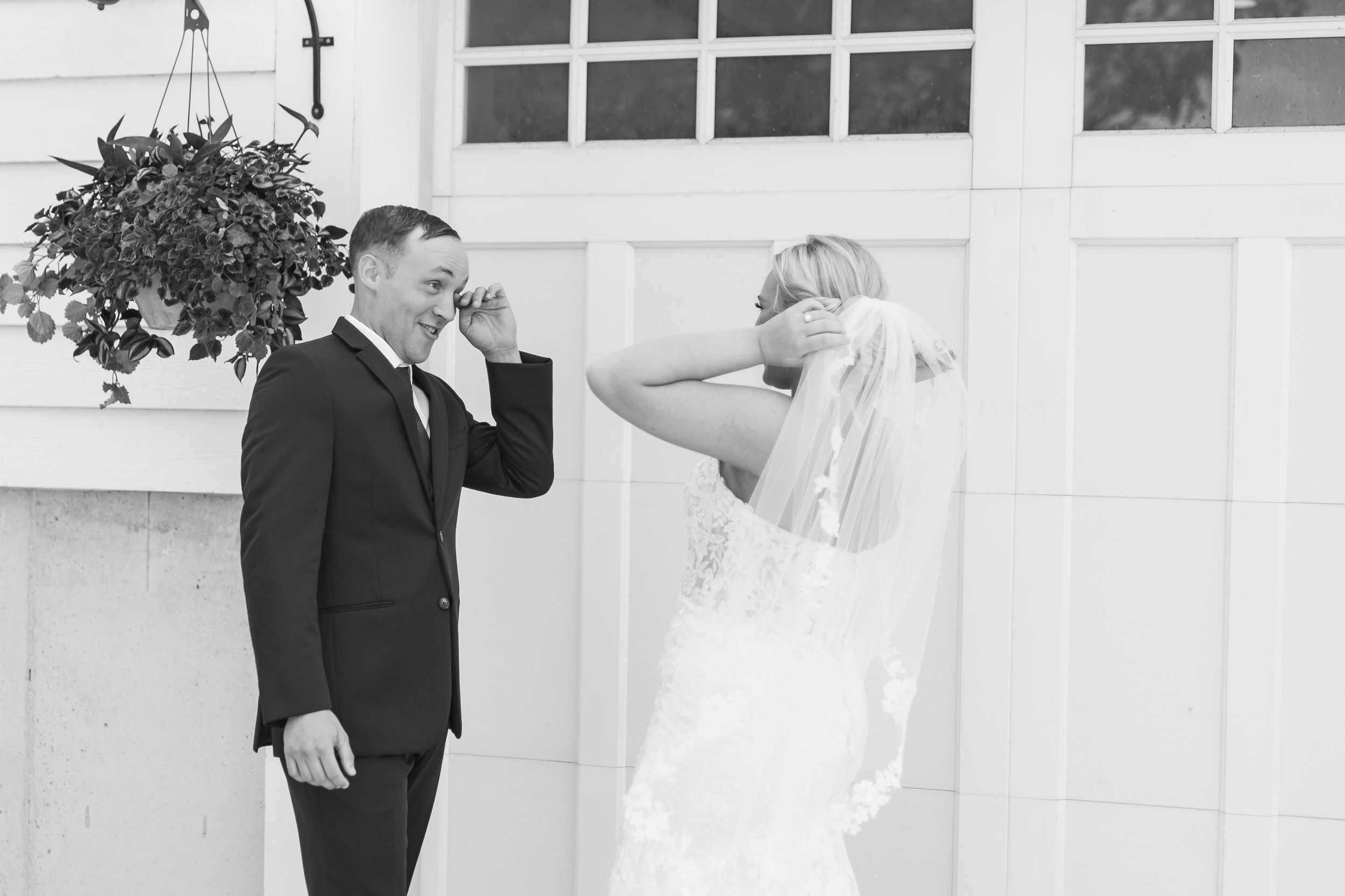 Black and white photo of emotional bride and groom sharing a first look moment outside a white building on their wedding day.