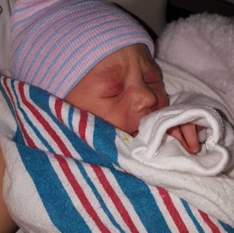 A newborn baby wearing a striped hat and blanket sleeps peacefully.