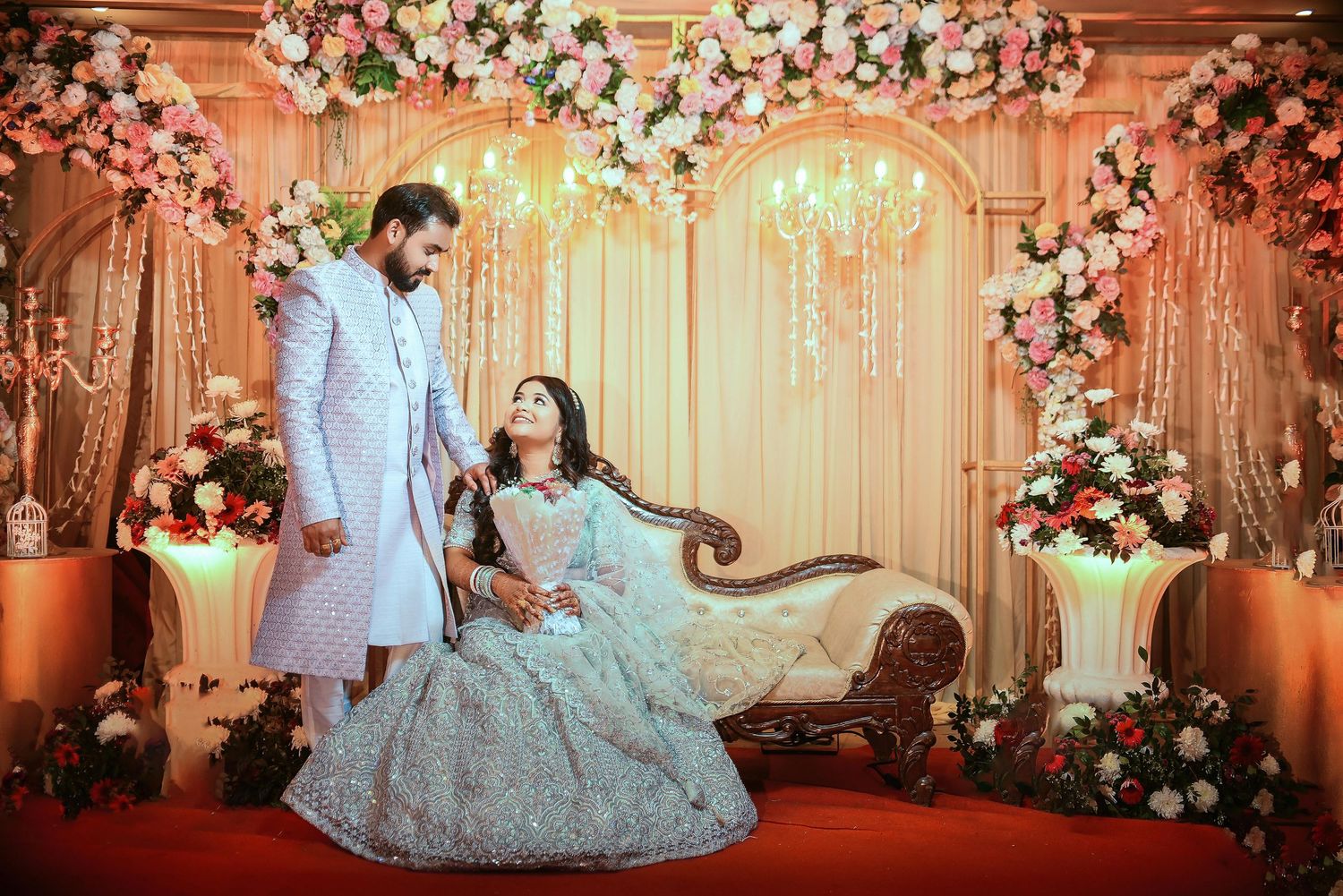 Elegant Indian wedding mandap decorated with pink and orange flowers, crystal chandeliers, and warm lighting.