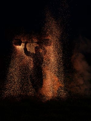 Silhouette d'un artiste avec une cage à charbon entourée d'une explosion spectaculaire d'étincelles dorées dans l'obscurité
