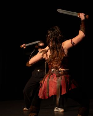 une escrimeuse artistique, vêtu d'un costume rouge de guerrière, brandissant deux épées sur scène lors d'un spectacle en direct.