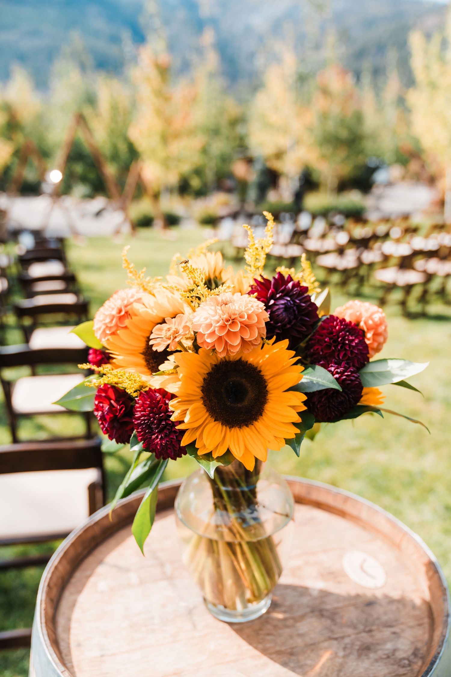 Fall wedding bouquet with sunflowers and burgundy dahlias in glass vase on wine barrel at outdoor ceremony. north cascades elopement wedding