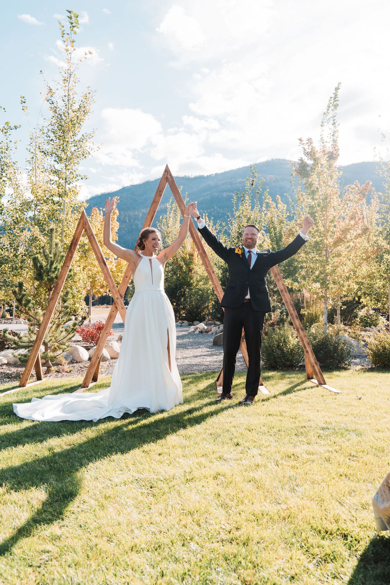 Bride and groom celebrate under wooden arch at outdoor mountain wedding ceremony on sunny day. north cascades elopement wedding