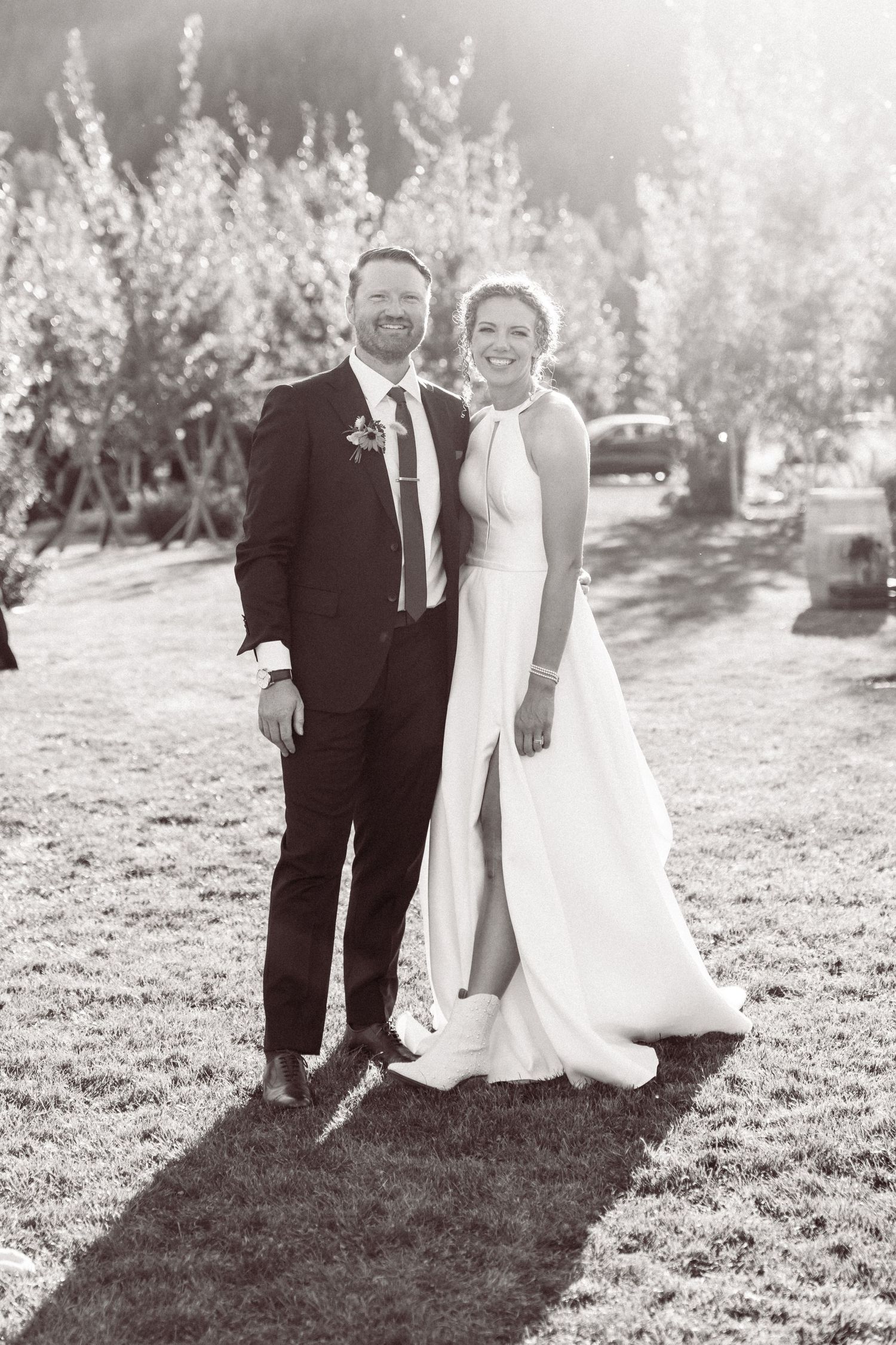 Black and white photo of a smiling bride and groom standing on grass outdoors on their wedding day.north cascades elopement wedding