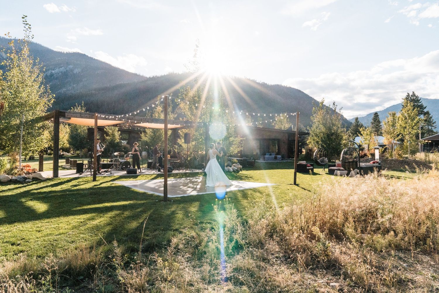 Outdoor mountain wedding venue with string lights, green lawn, and sun flare over scenic peaks. north cascades elopement wedding
