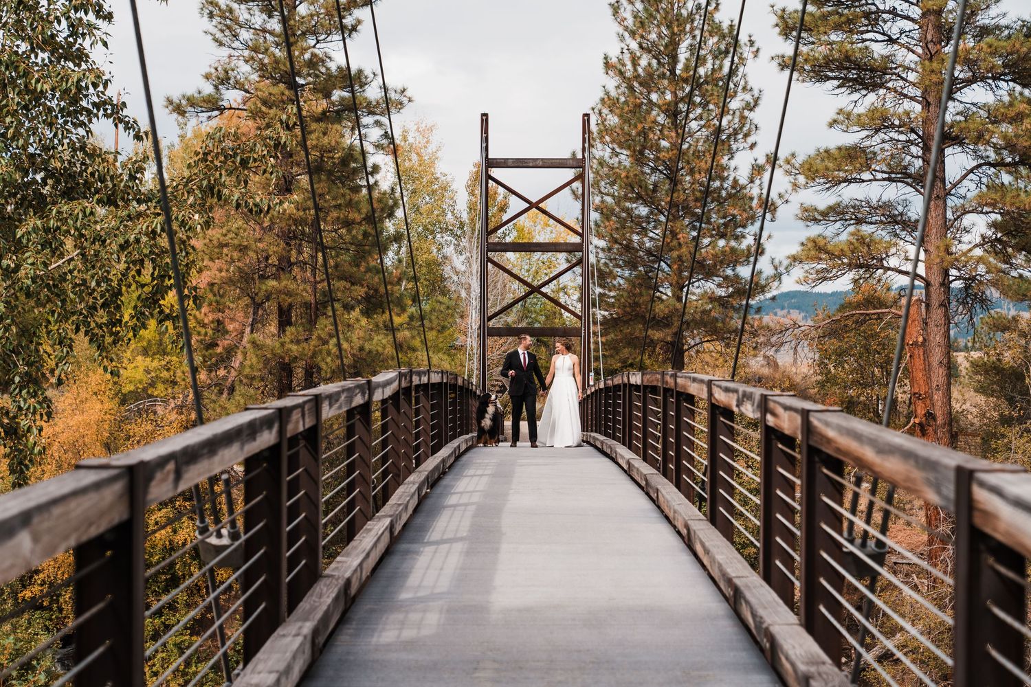 Bride and groom pose on rustic suspension bridge surrounded by autumn foliage at mountain wedding.north cascades elopement wedding