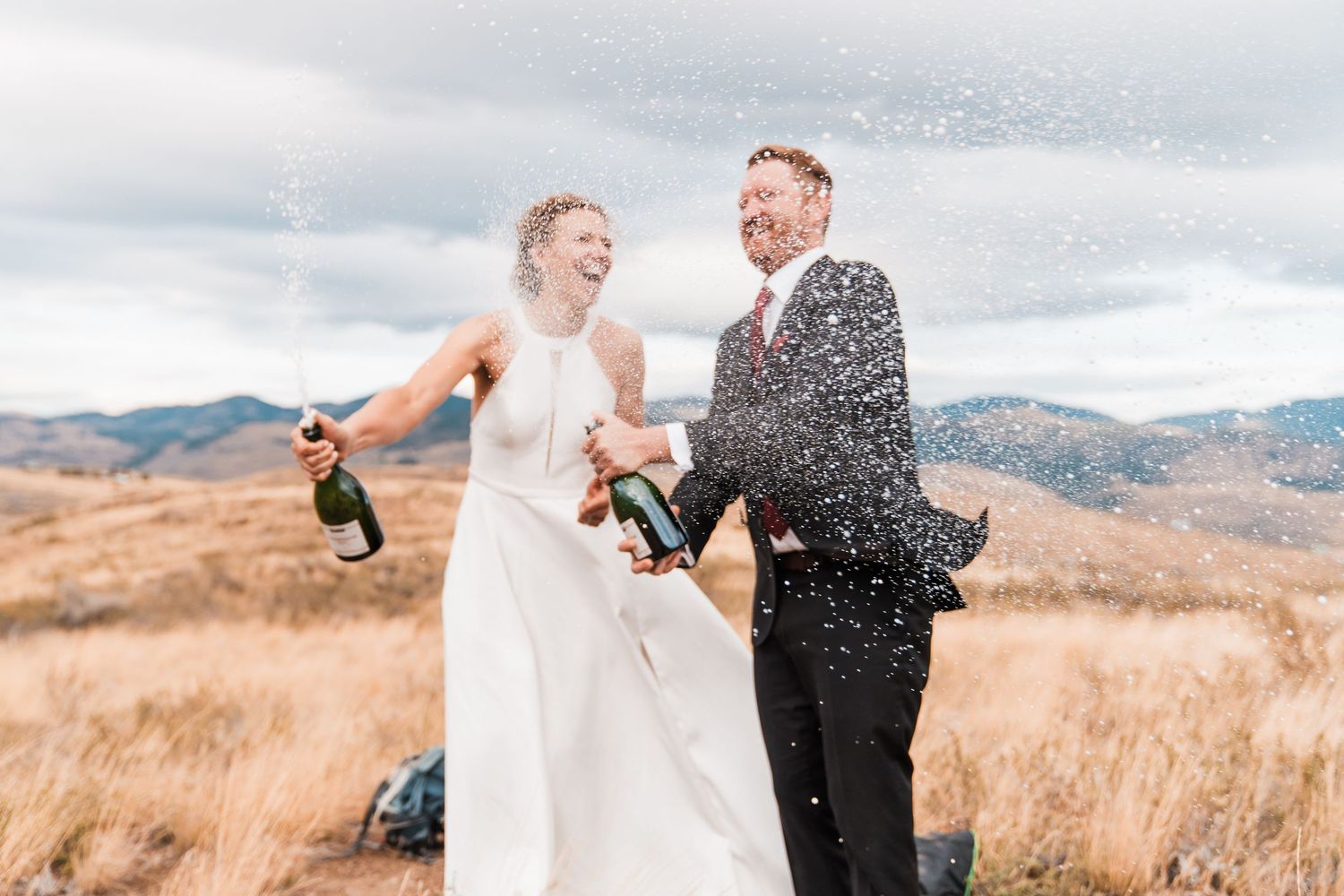 Joyful bride and groom pop champagne bottles on a scenic mountain hilltop, celebrating their wedding day. north cascades elopement wedding