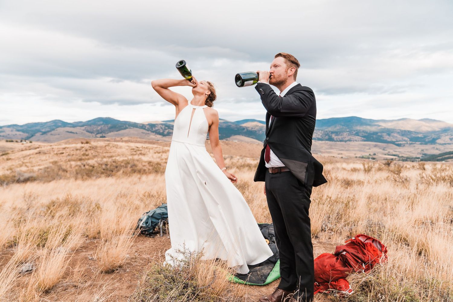 Bride and groom drink from bottles on a mountain hilltop with scenic valley views. north cascades elopement wedding