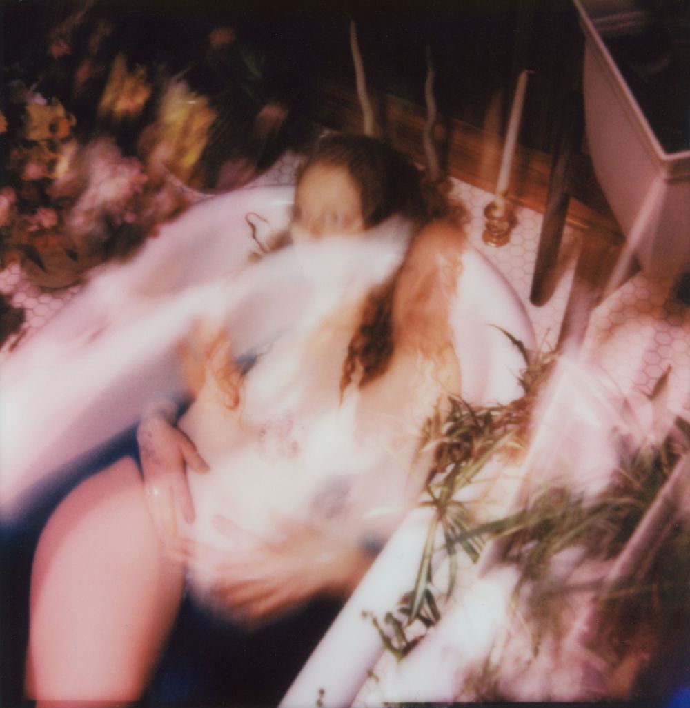 Blurry artistic Polaroid photo of a person lying among flowers with a dreamy, ethereal double-exposure effect.