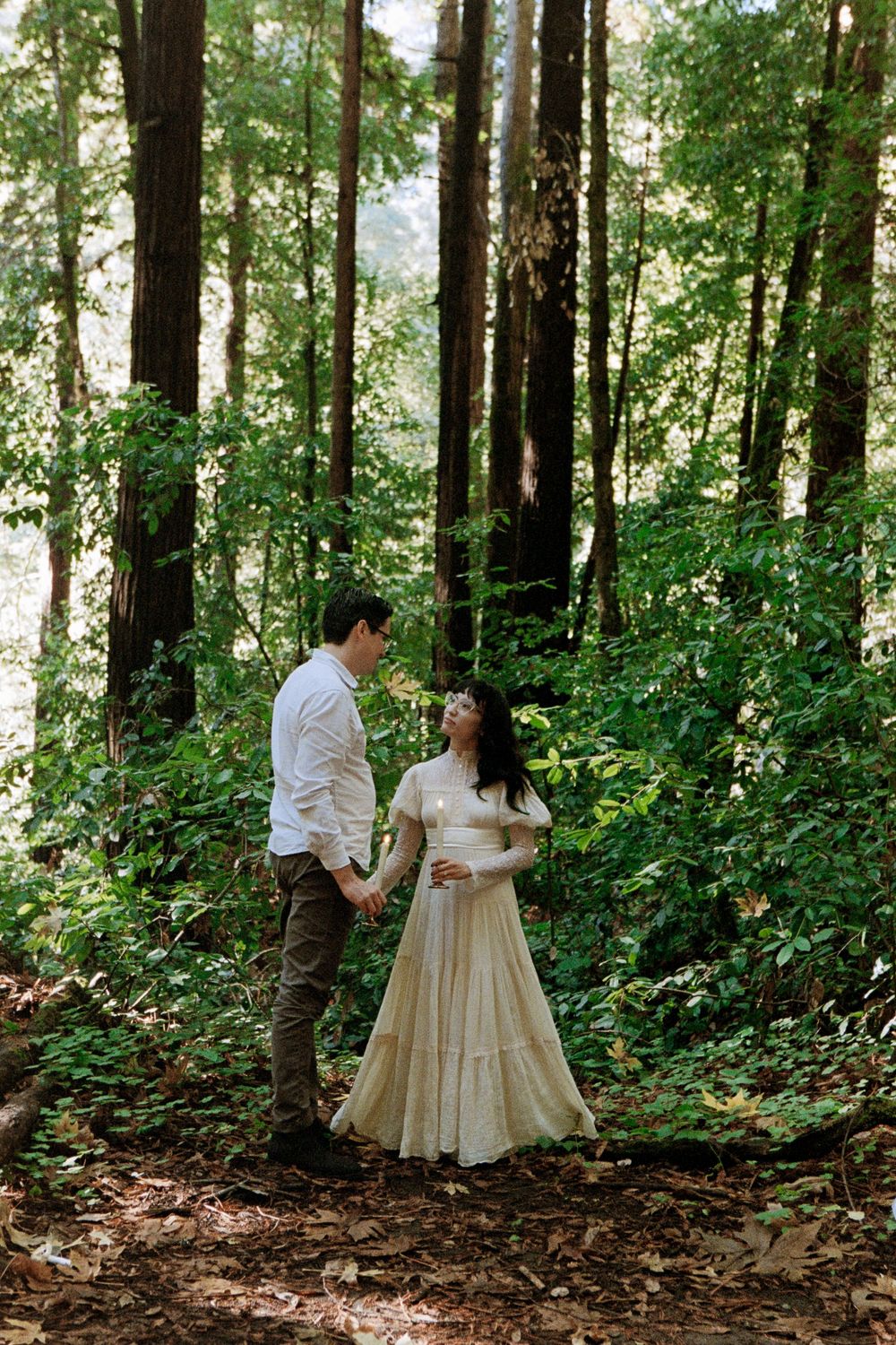 Couple holding hands and gazing at each other in a redwood forest.