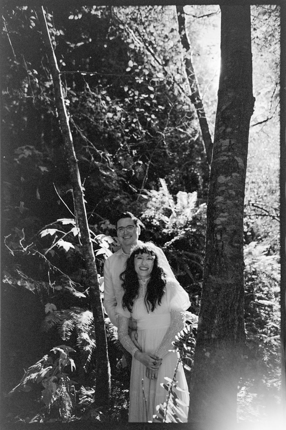 Couple smiling together in a lush forest, black and white engagement photo.