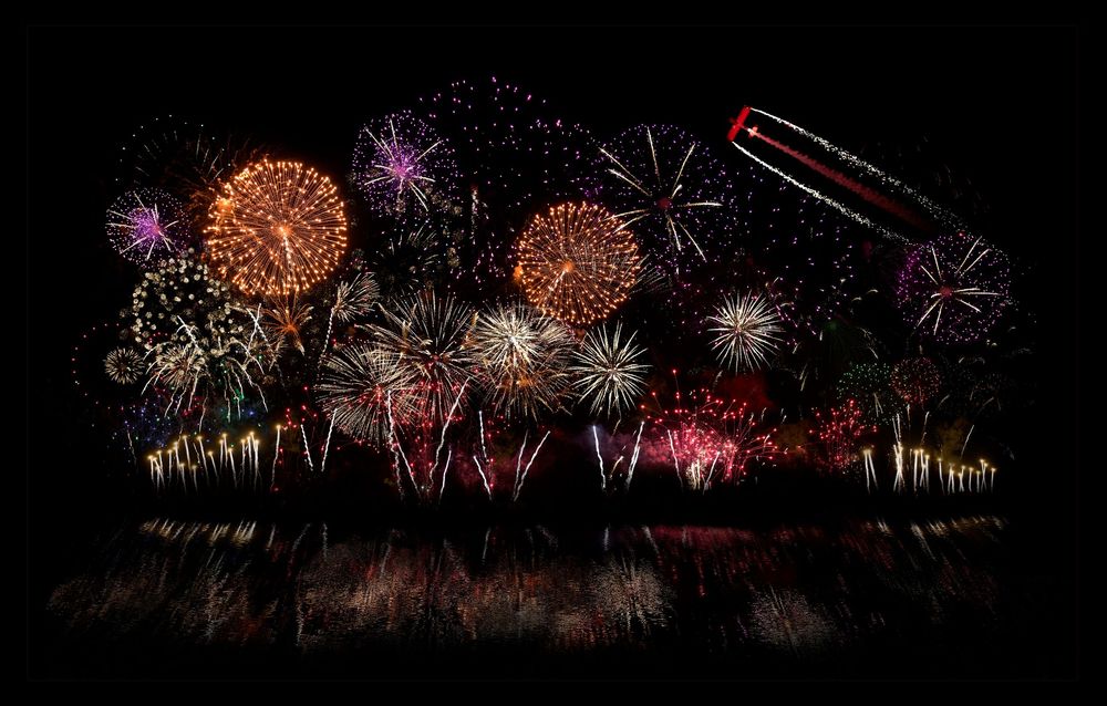 Vibrant red, gold and purple fireworks illuminate the night sky over a dark horizon during a spectacular pyrotechnic display.