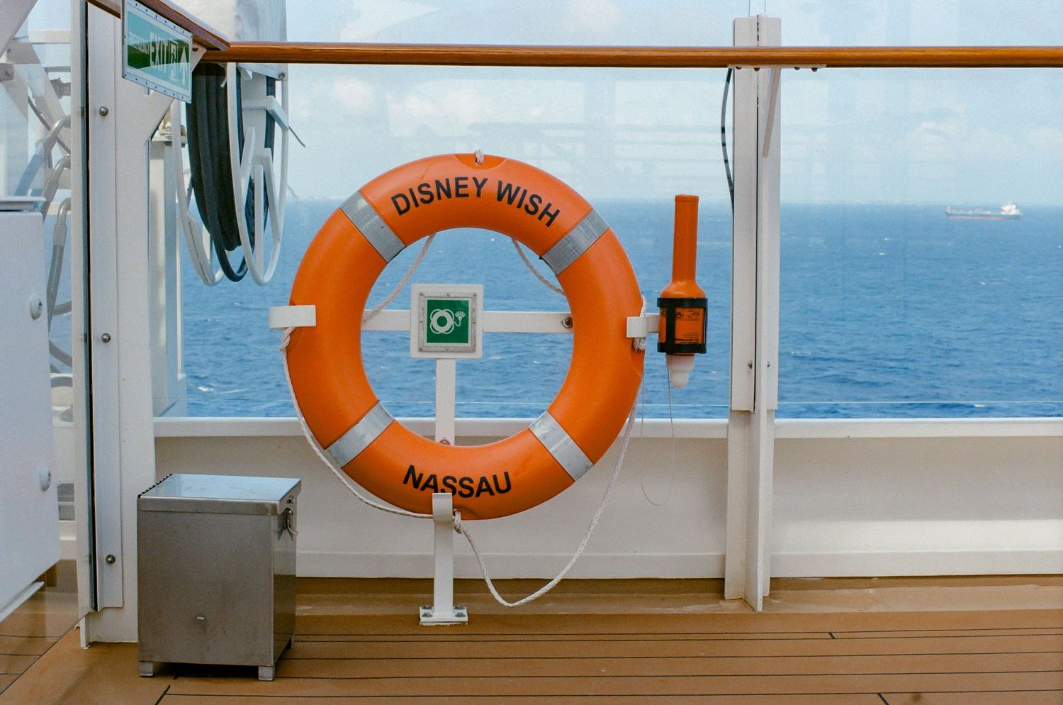 Orange Disney Wish Nassau life preserver ring mounted on cruise ship deck railing with ocean view.
