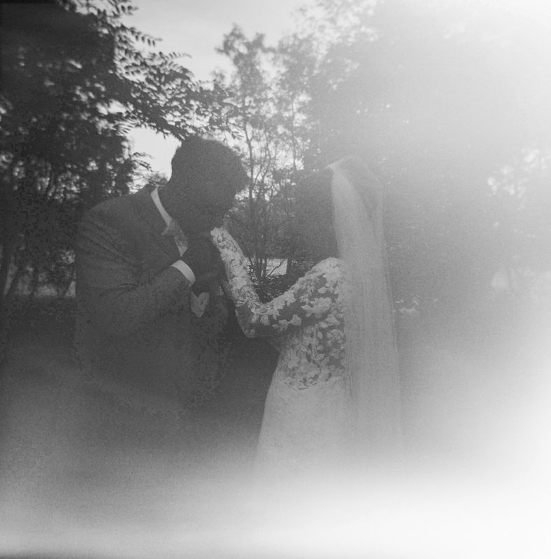 Black and white vintage wedding photo of bride and groom sharing a kiss outdoors, surrounded by trees.