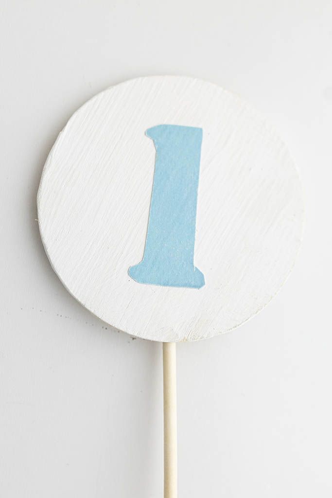 White circular wooden cake topper with light blue number 1 for first birthday celebration.